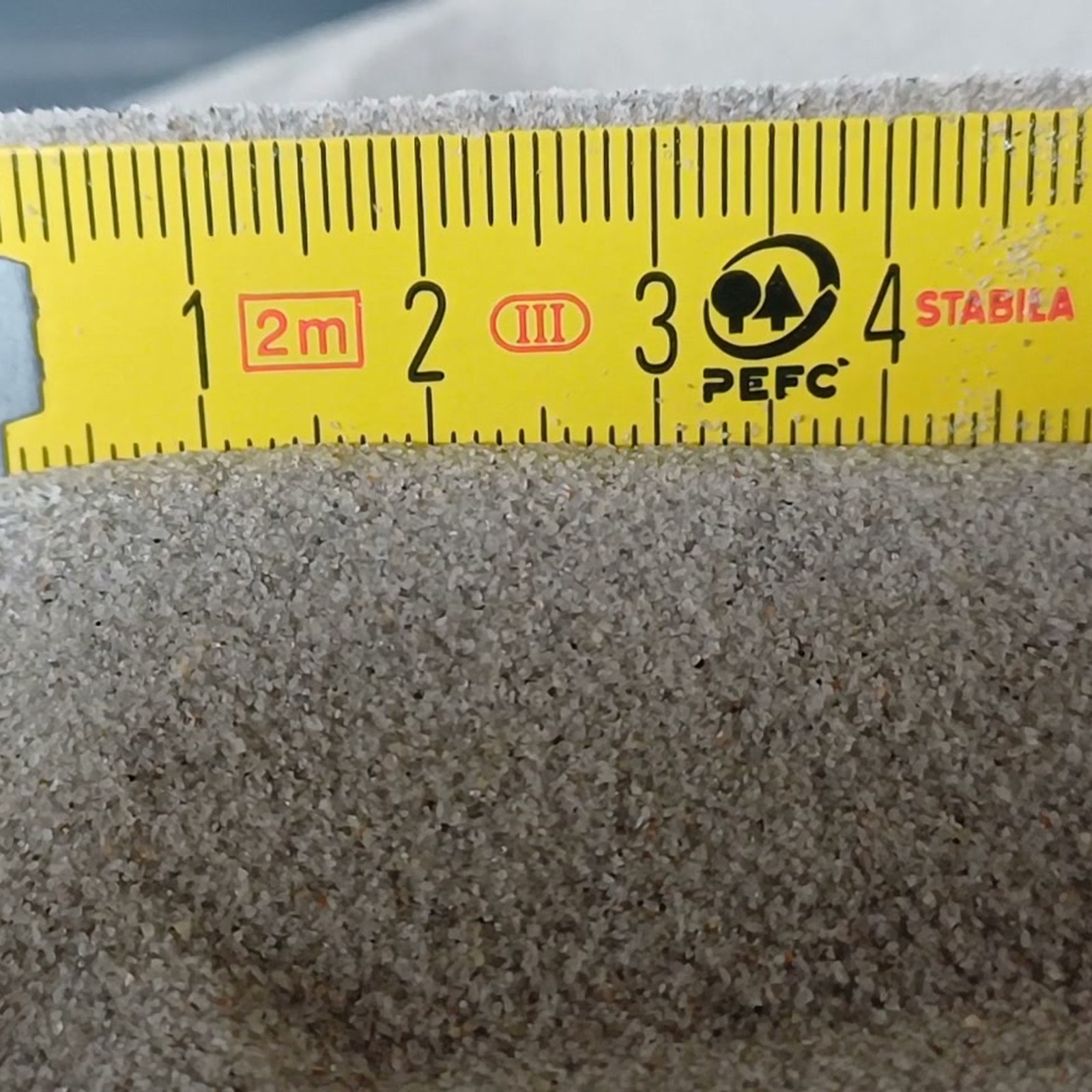 Chinchillasand Naturgrau, 0,1–0,3 mm, 10 kg: Erhöhte Sandkante direkt vor einem gelben Gliedermaßstab.
