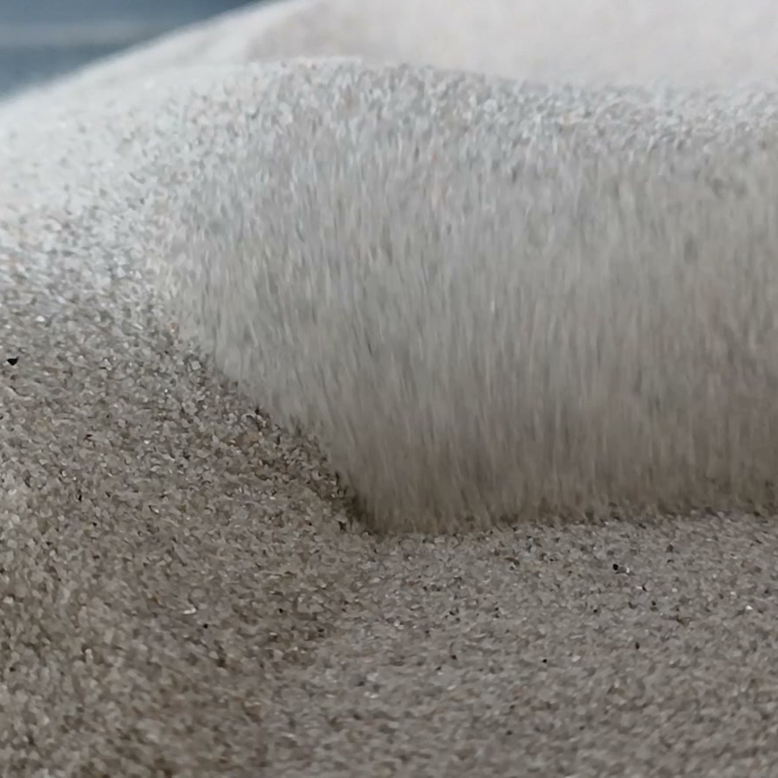 Chinchillasand Naturgrau, 0,1–0,3 mm, 5 kg: Nahaufnahme einer steilen grauen Sandkante.