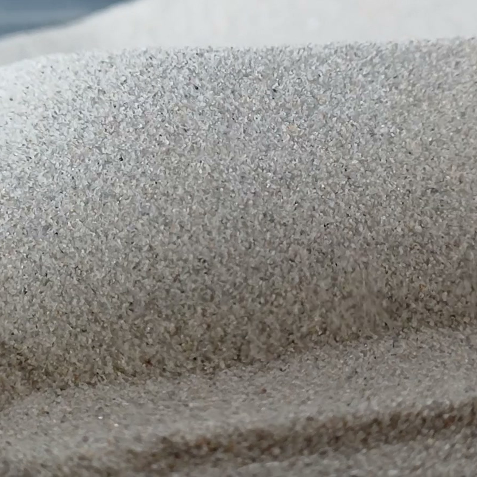 Chinchillasand Naturgrau, 0,1–0,3 mm, 5 kg: Zwei graue Sandrücken mit einer Rinne dazwischen.