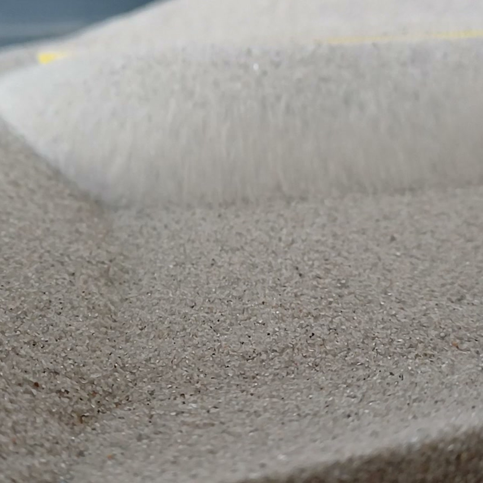 Chinchillasand Naturgrau, 0,1–0,3 mm, 5 kg: Flache Sandfläche vor hohem Sandrand.