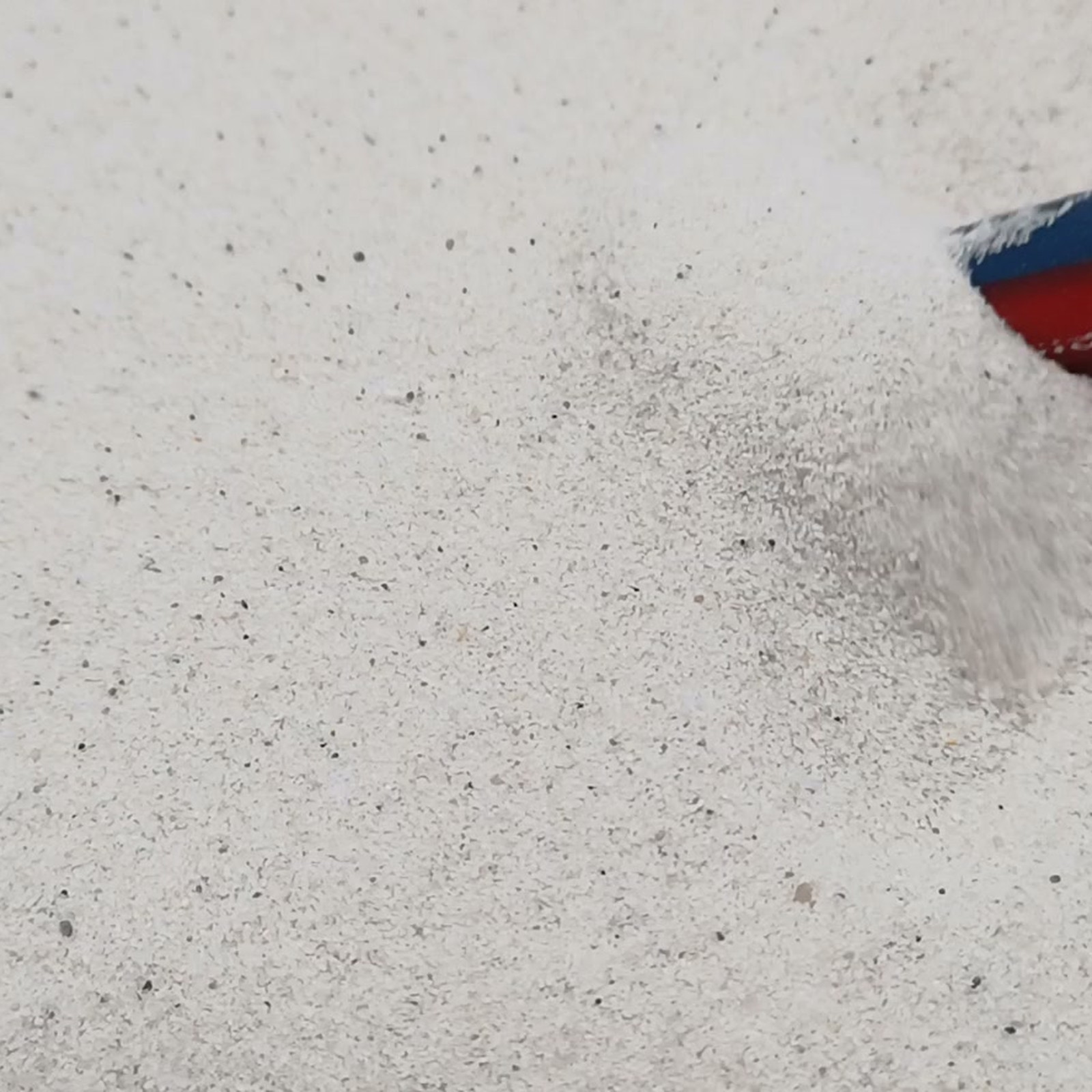 Feine weiße Sandkörner mit dunklen Sprenkeln und einer kleinen Mulde – Quarzsand Naturweiß für das Aquarium, 0,1–0,4 mm, 25 kg.