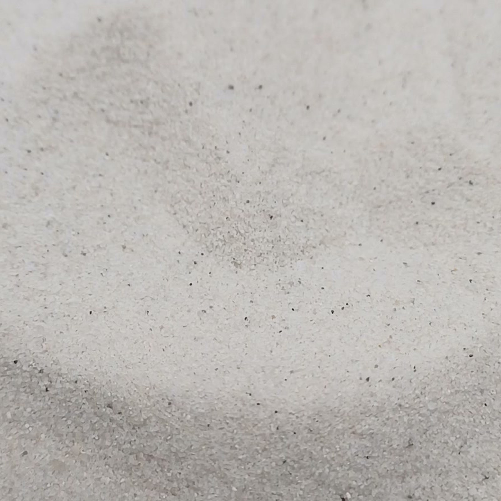 Geschwungene Vertiefung im hellen Sand mit dunklerem Rand im Vordergrund – Quarzsand Naturweiß für das Aquarium, 0,1–0,4 mm, 25 kg.