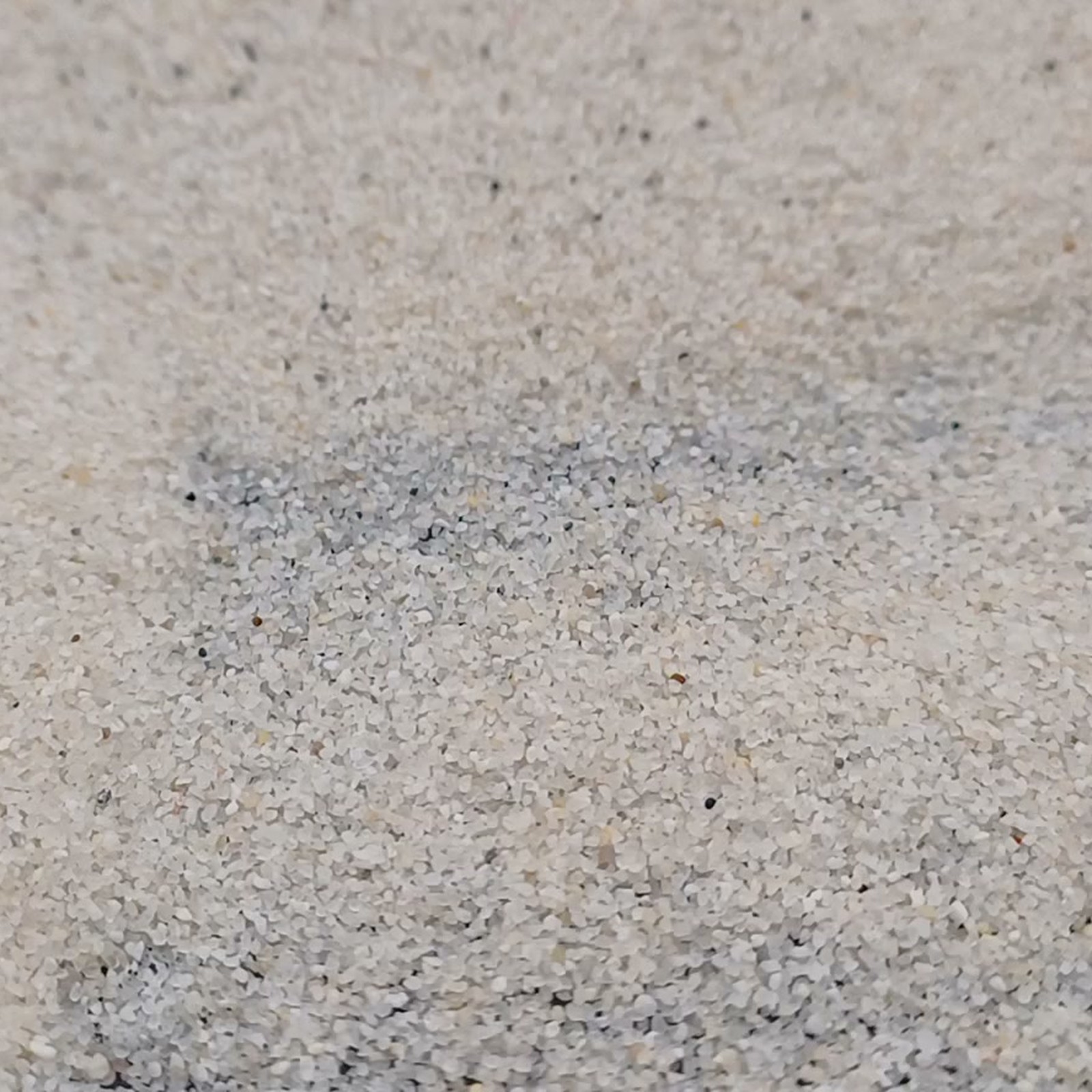 Aquariumsand Naturweiß, 0,2–0,5 mm, 25 kg: Flache Kornfläche mit dünn bedeckter dunkler Stelle.