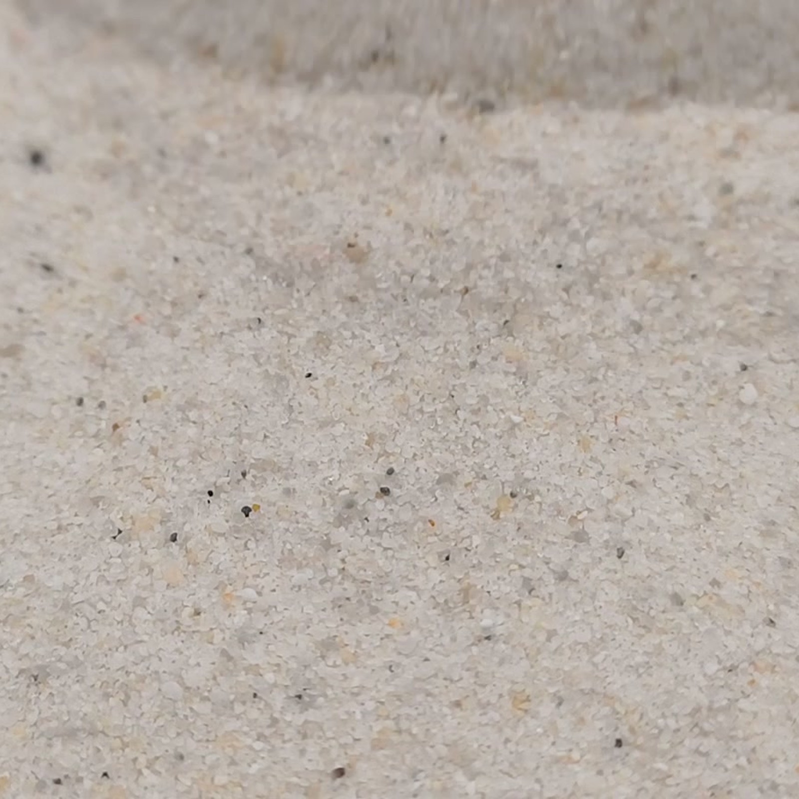 Industriesand Naturweiß, 0,1–0,6 mm, 25 kg: Helle Kornfläche mit dunklen Einzelkörnern.