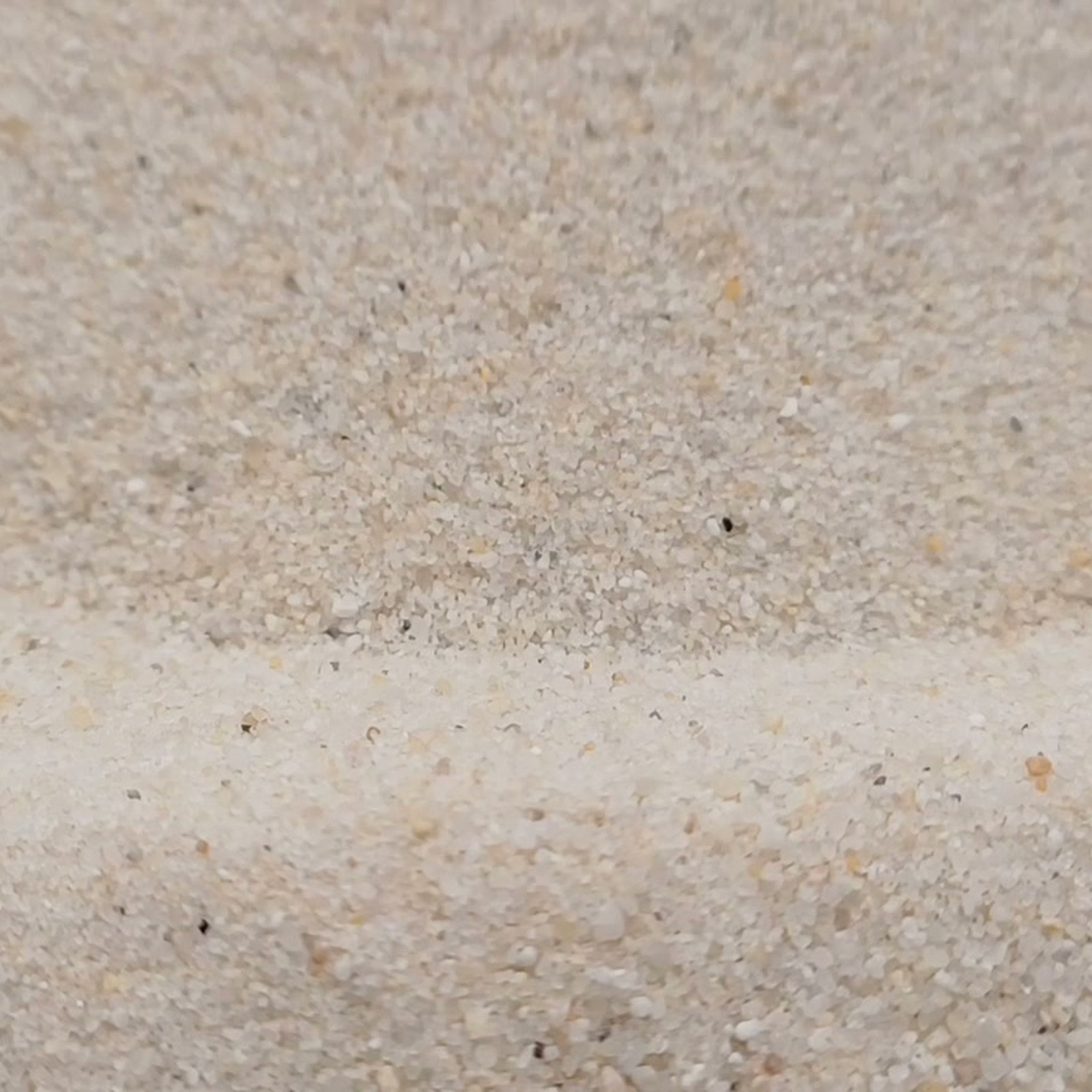 Industriesand Naturweiß, 0,1–0,6 mm, 25 kg: Kornstruktur an zwei niedrigen Sandwellen.
