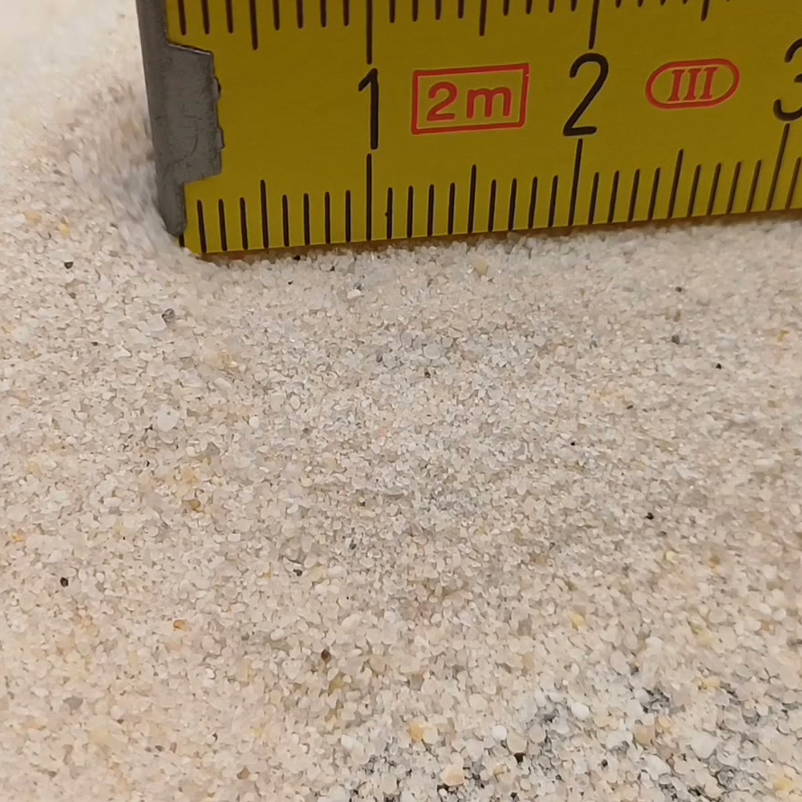 Industriesand Naturweiß, 0,1–0,6 mm, 25 kg: Sandkörner vor dem Ende eines gelben Maßstabs.