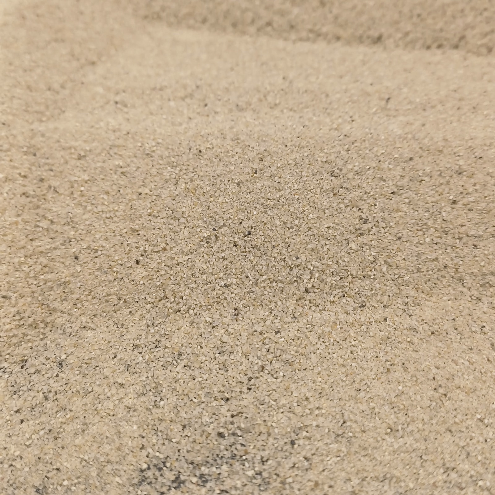 Aquariumsand Naturbeige, 0,1–0,5 mm, 6,3 kg: Beige Kornfläche mit dunklerem Untergrund am Bildrand.