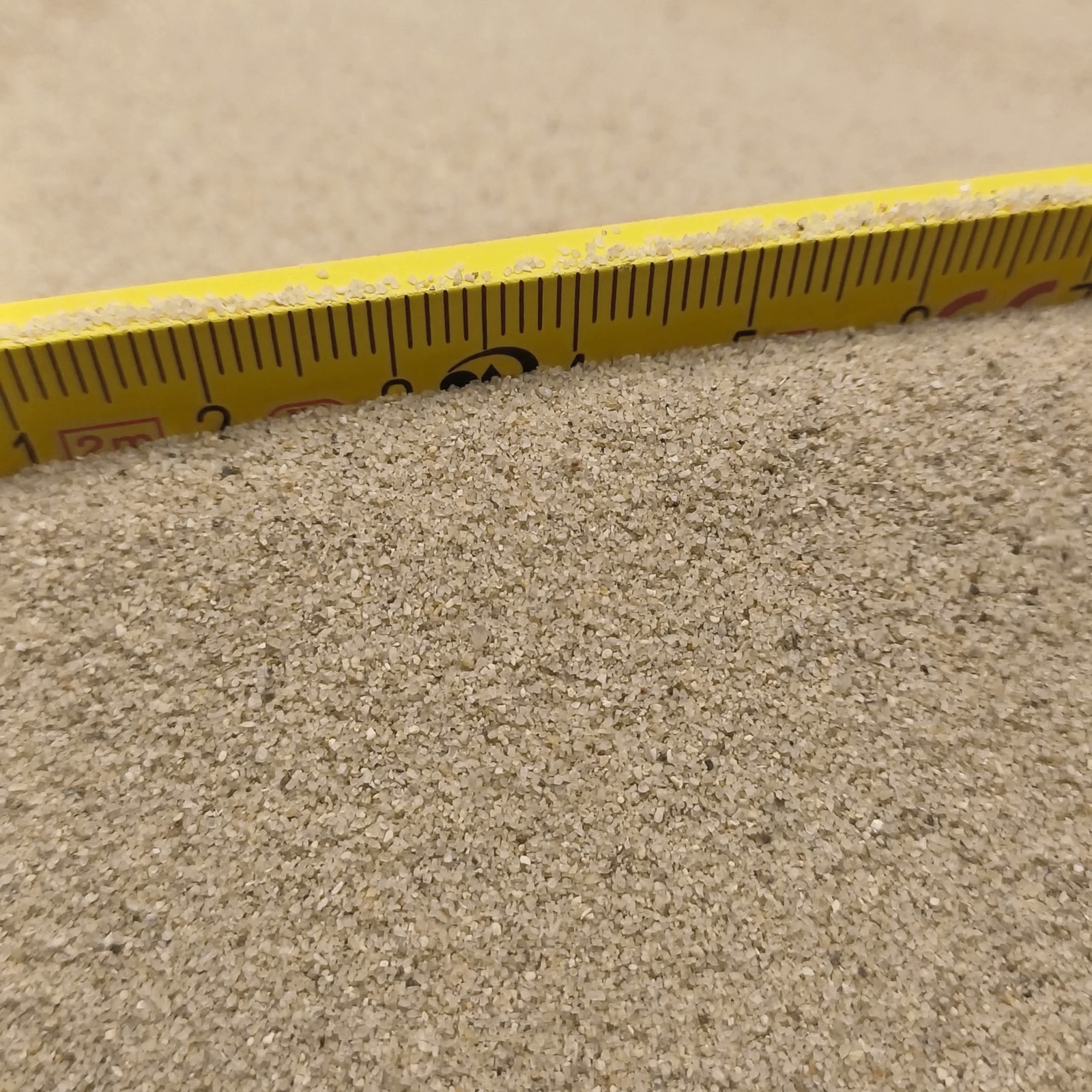 Aquariumsand Naturbeige, 0,1–0,5 mm, 6,3 kg: Sandfläche direkt unter einem gelben Gliedermaßstab.