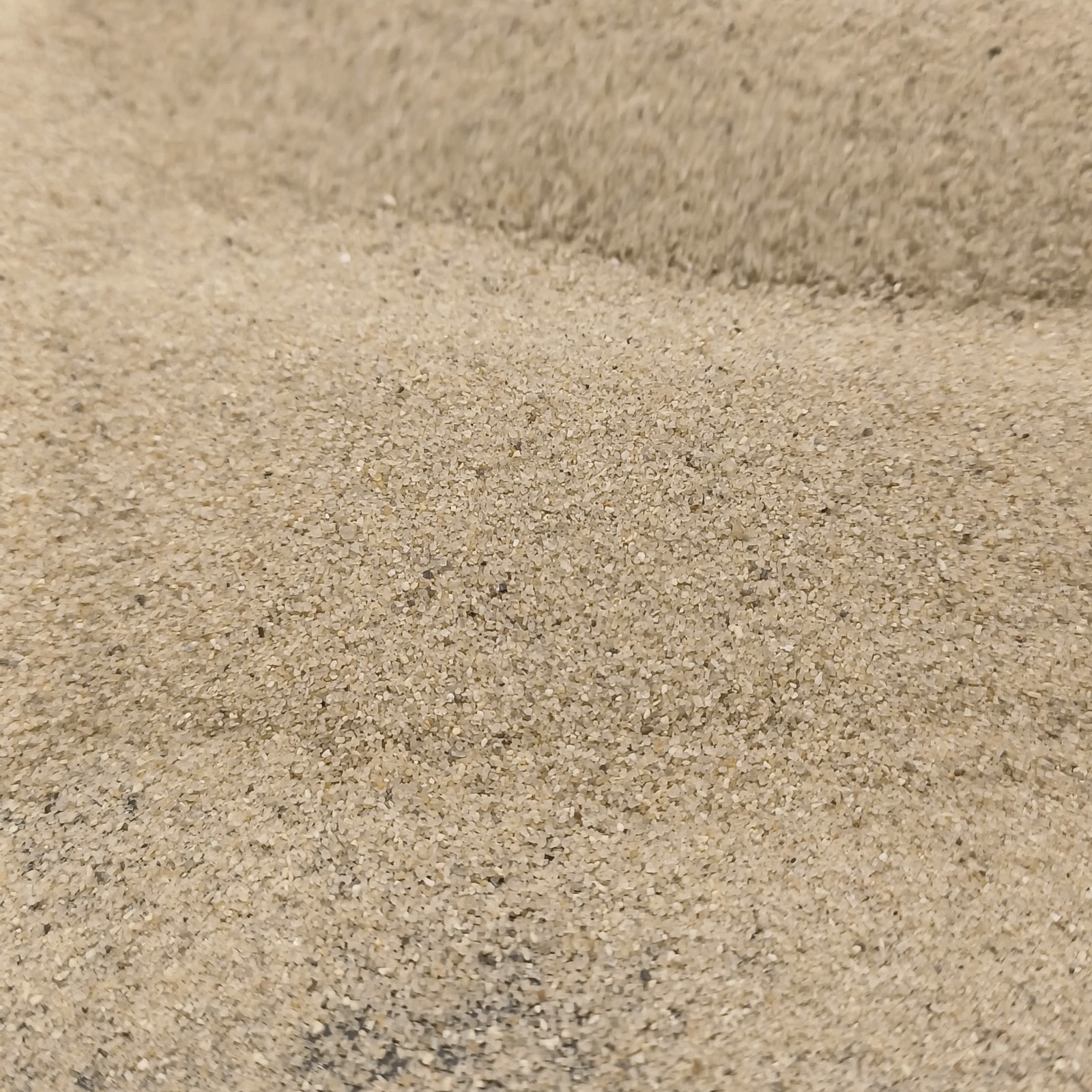 Aquariumsand Naturbeige, 0,1–0,5 mm, 7,5 kg: Beige Sandkörner vor einer erhöhten Kante.