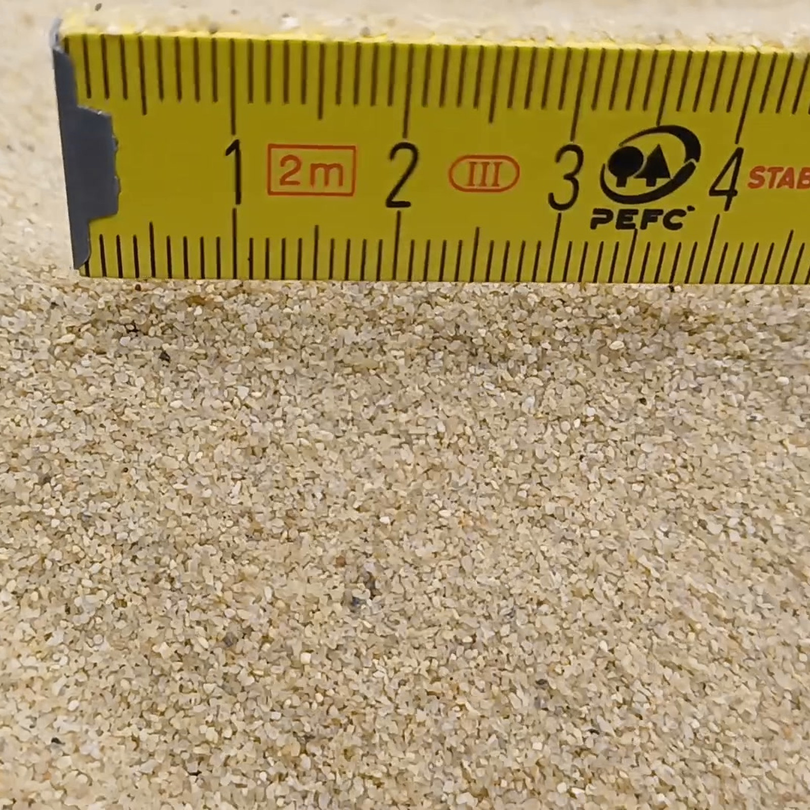 Aquariumsand Naturbeige, 0,2–0,7 mm, 10 kg: Sandkörner unmittelbar vor dem gelben Maßstab.