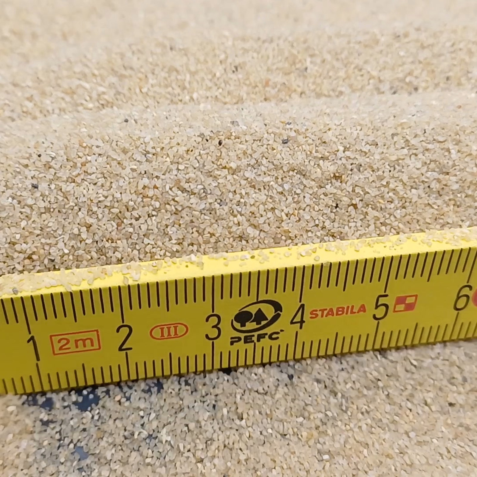 Aquariumsand Naturbeige, 0,2–0,7 mm, 10 kg: Sandwellen hinter einem gelben Gliedermaßstab.