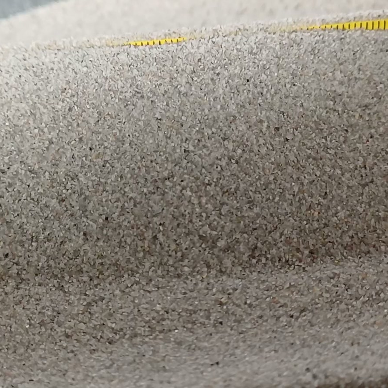 Aquariumsand Naturgrau, 0,1–0,5 mm, 10 kg: Kornstruktur an einer Sandkante unter einem Maßstab.