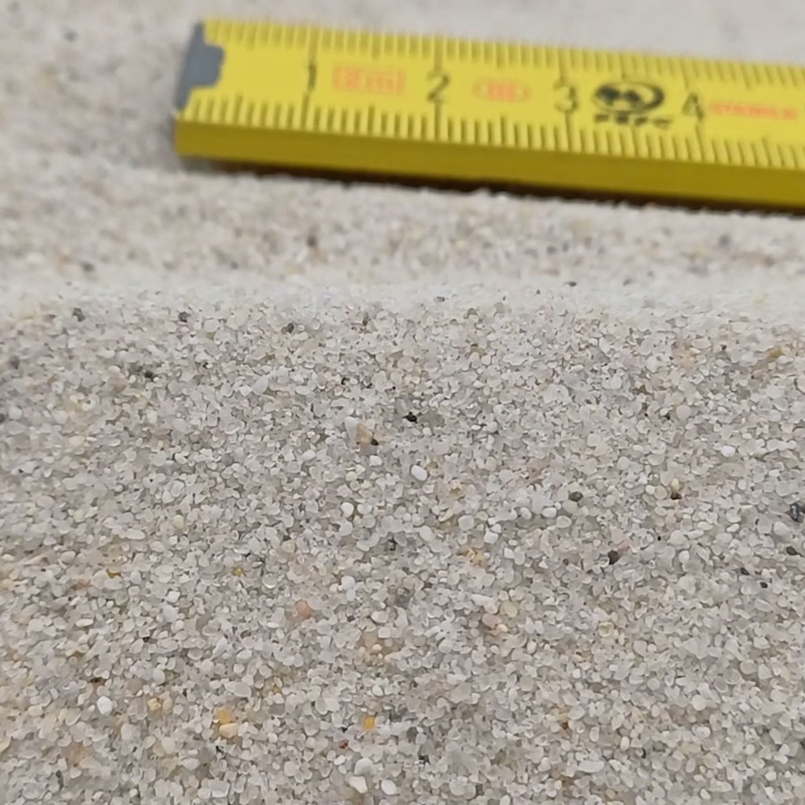 Vogelsand Naturweiß, 0,2–0,8 mm, 14 kg: Sandwelle vor liegendem gelbem Maßstab.