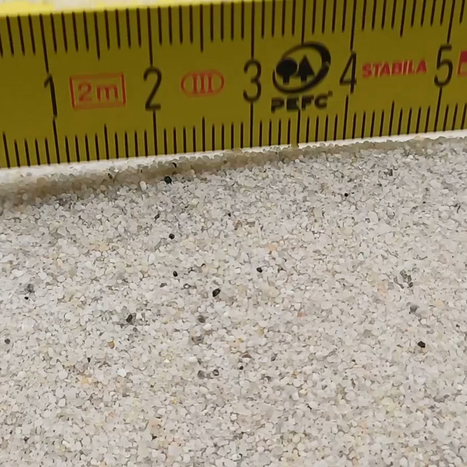 Vogelsand Naturweiß, 0,2–0,8 mm, 19 kg: Kornstruktur direkt vor dem aufgestellten Maßstab.