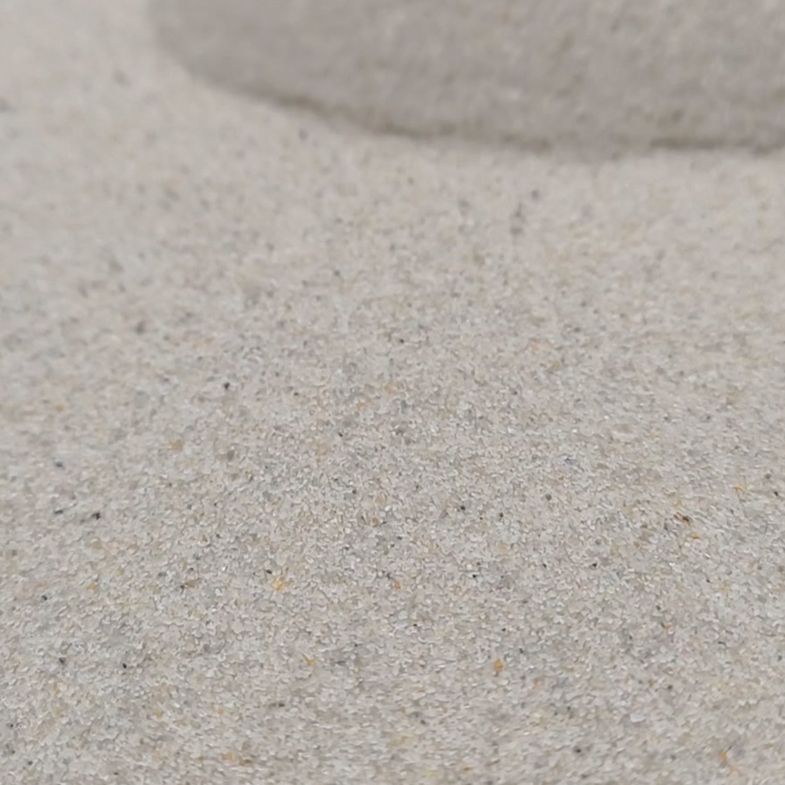 Chinchillasand Naturbeige, 0,1–0,3 mm, 25 kg: Feine Sandfläche vor einer erhöhten hinteren Kante.