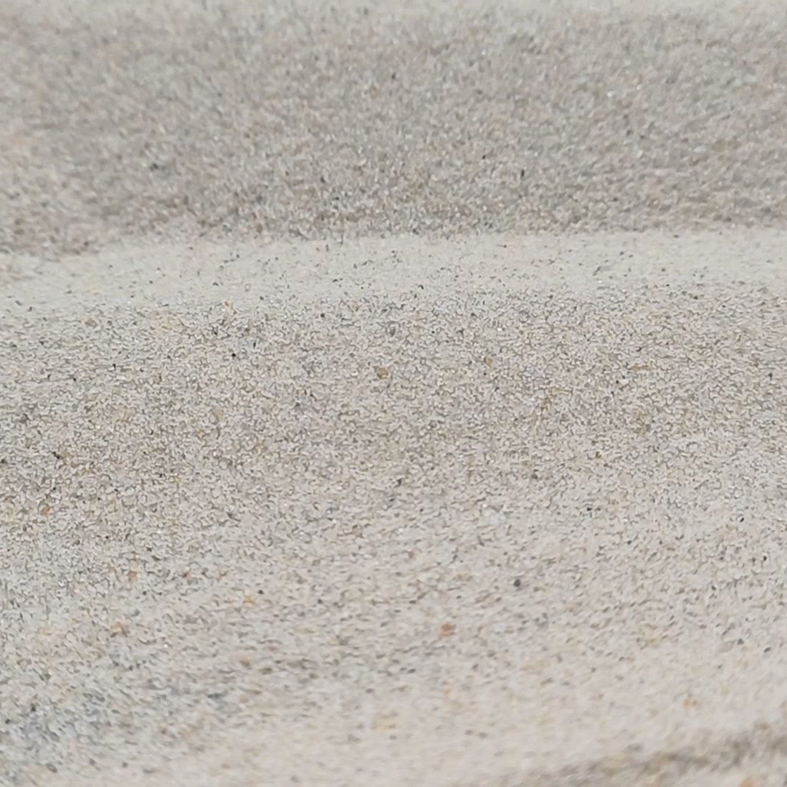 Chinchillasand Naturbeige, 0,1–0,3 mm, 25 kg: Körnige Fläche unter einer erhöhten Sandkante.