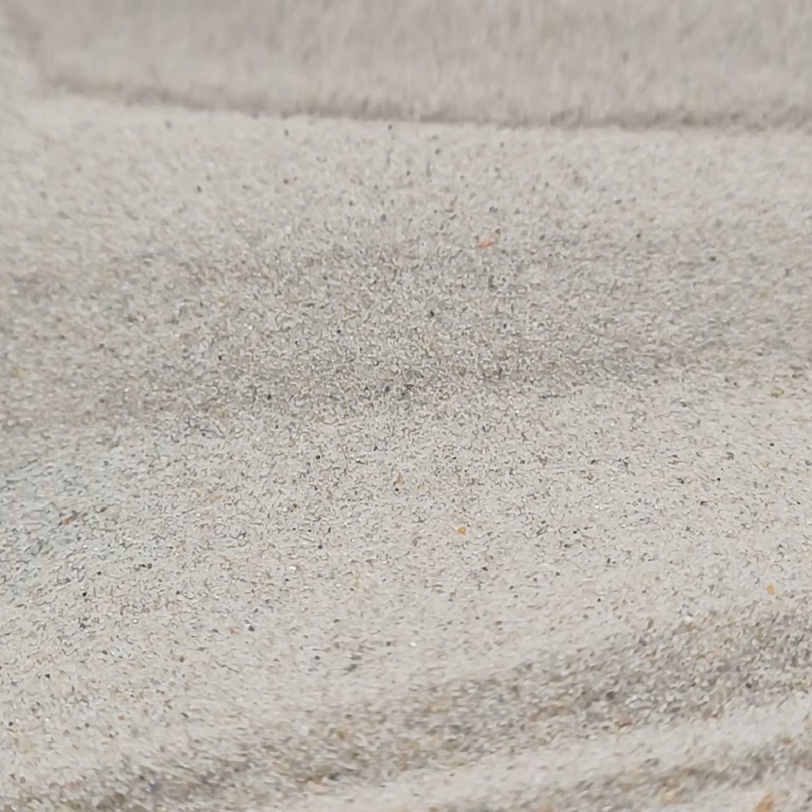 Chinchillasand Naturbeige, 0,1–0,3 mm, 25 kg: Beige Sandoberfläche mit geschwungener Rinne.