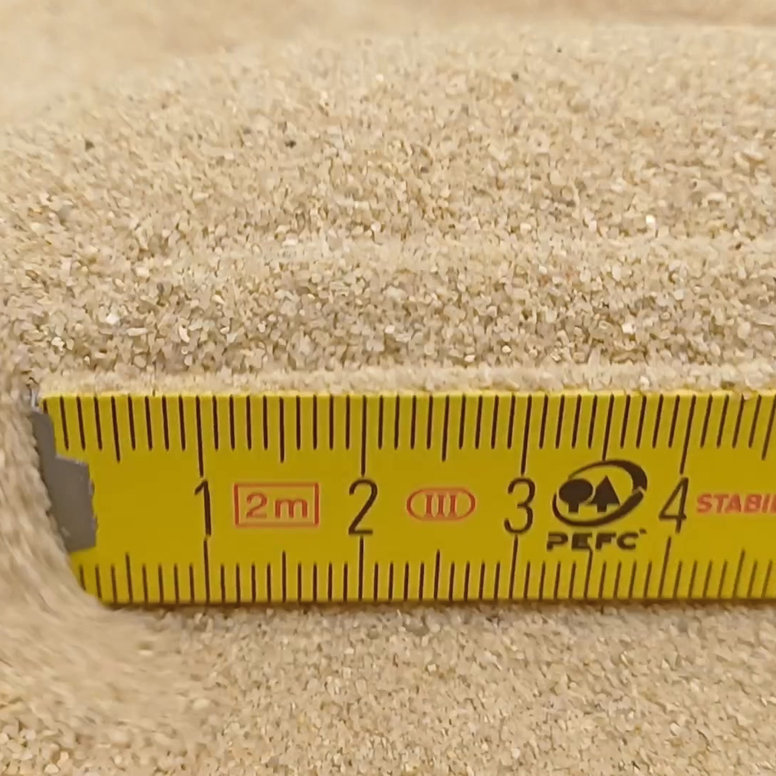 Aquariumsand Naturbeige, 0,1–0,6 mm, 25 kg: Beige Sandkörner hinter einem gelben Maßstab.