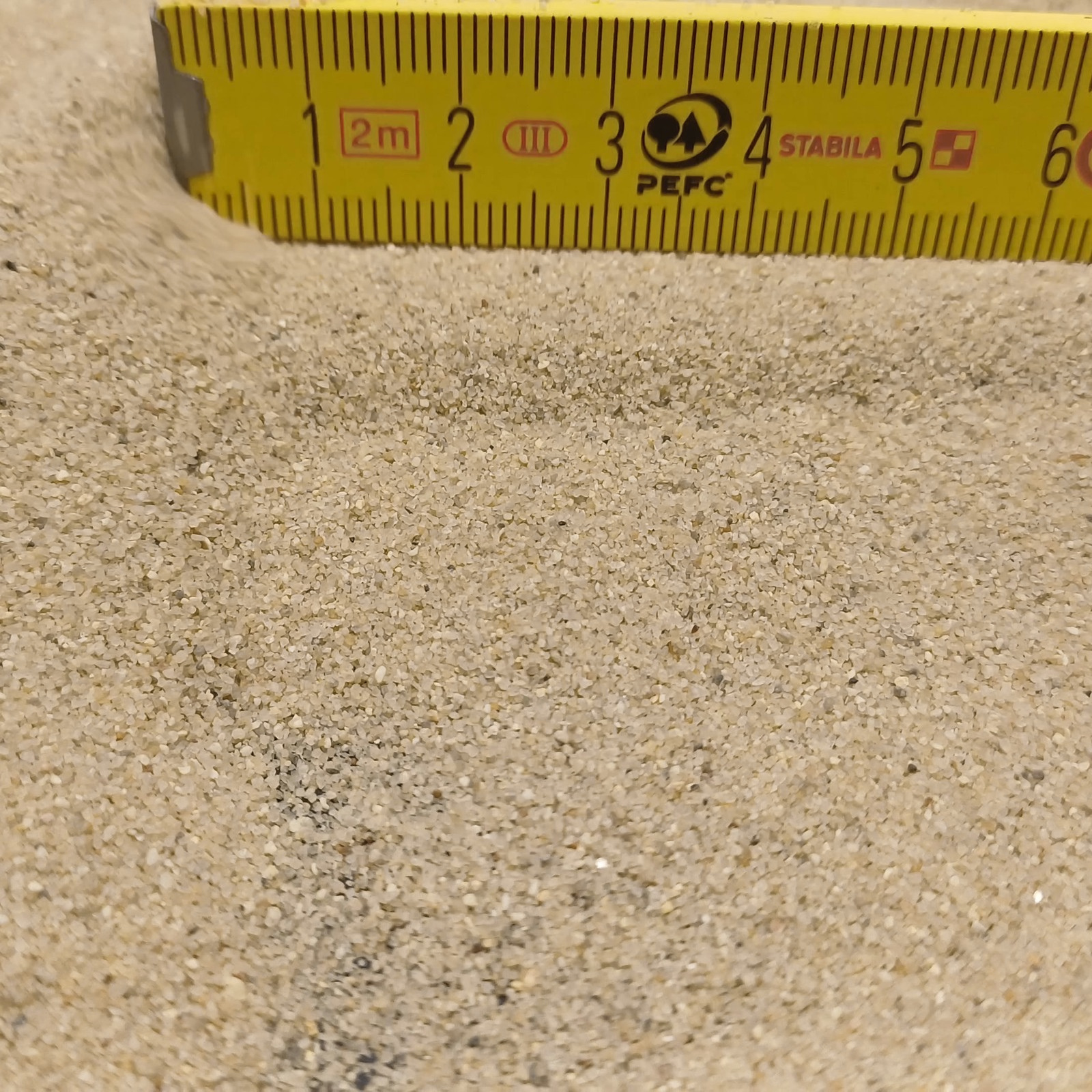 Terrariumsand Naturbeige, 0,3–0,6 mm, 25 kg: Kornfläche vor einem gebogenen gelben Maßstab.