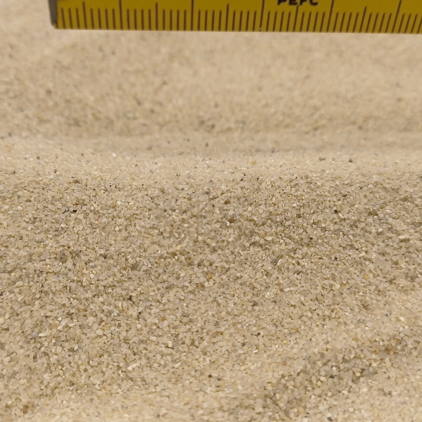 Terrariumsand Naturbeige, 0,3–0,6 mm, 25 kg: Zwei Sandwellen unter einem gelben Maßstab.